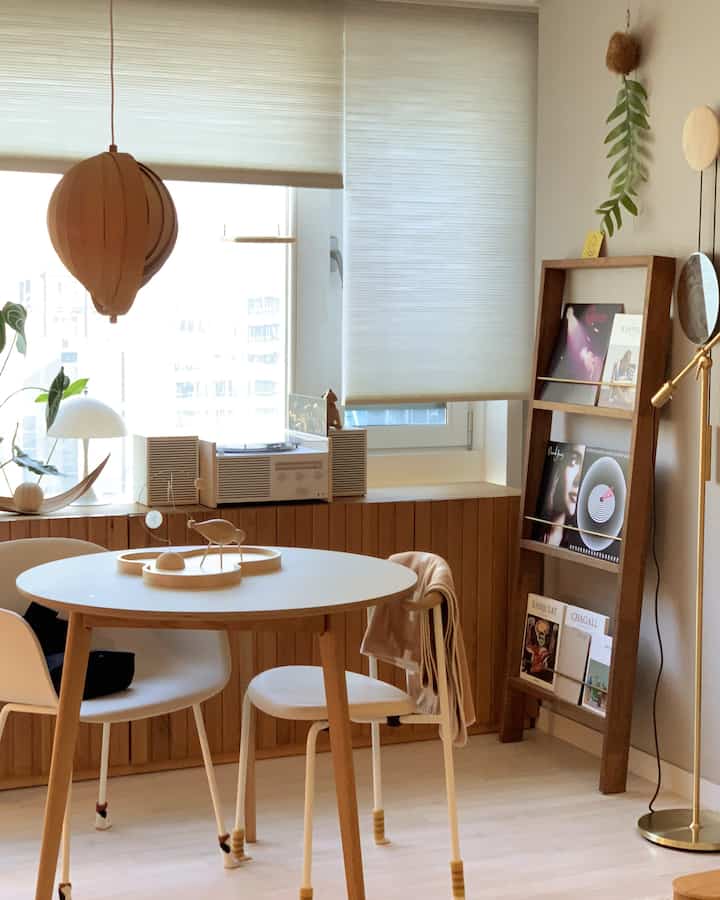 白と木目調が調和した北欧風のリビング、丸いダイニングテーブルとマガジンラック、暖かな照明が配置された雰囲気のあるインテリア