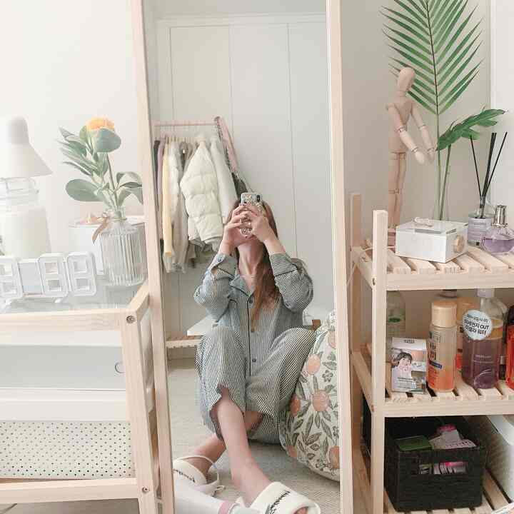 A natural-toned small bedroom featuring a large mirror, wooden storage shelves, and cushions creating a cozy selfie zone