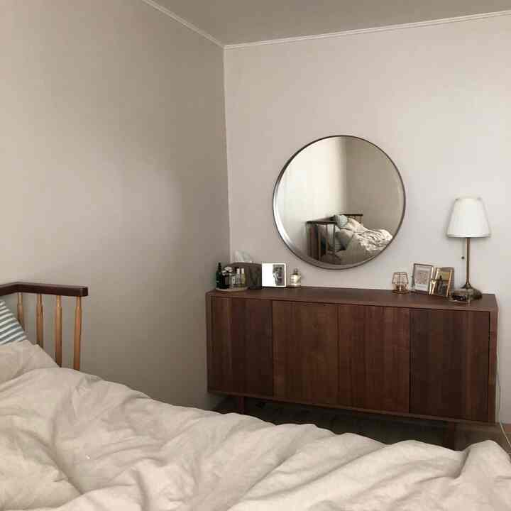 ナチュラルカラーと木目調が調和したシンプルな寝室、丸い鏡と木製チェストが配置され落ち着いた雰囲気のインテリア