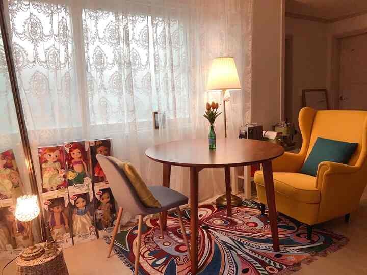 Bright yellow armchair and round dining table in cozy two-person dining room with lace curtains