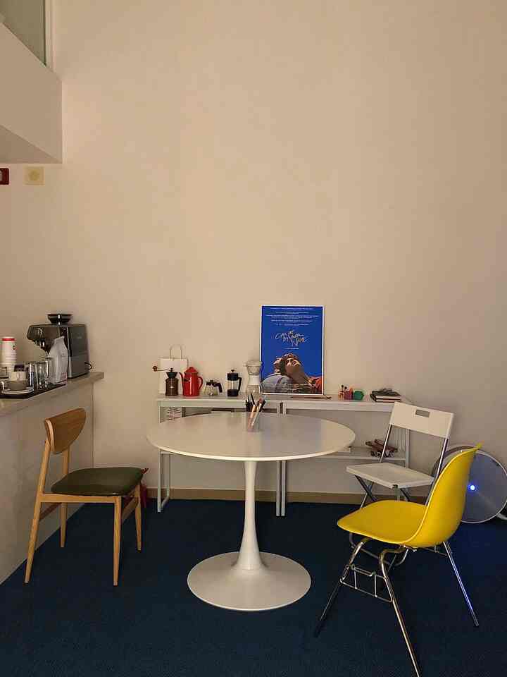 白と青のトーンの円形の部屋、中央に円形のテーブルと多様な椅子が配置されたミニマルで落ち着いたおうちカフェの空間