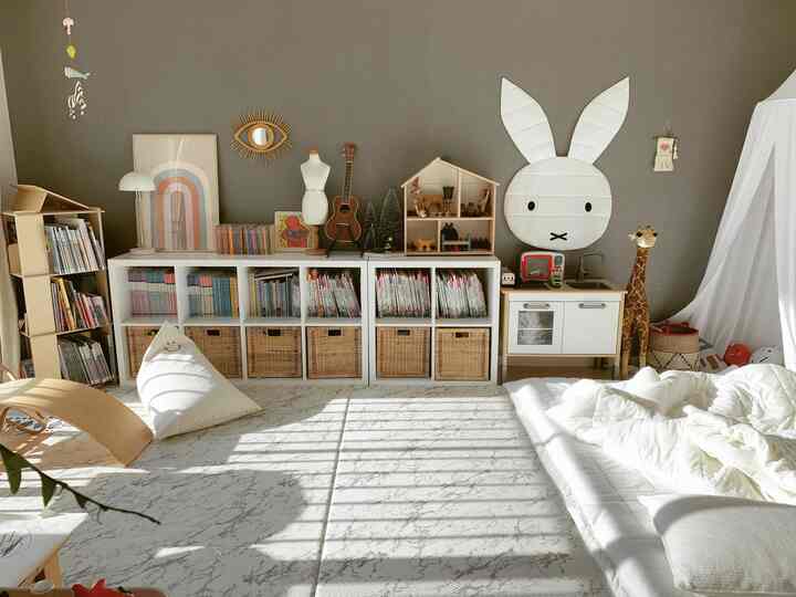 Natural-toned kids' room play area featuring bookshelves, storage baskets, toys, and a large rug with warm light and cozy atmosphere