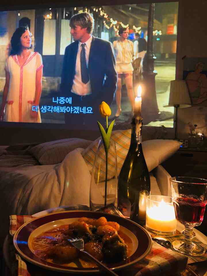 Cozy home cinema space with warm lighting and bedspread, featuring a table decorated with wine and candles