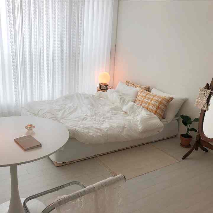 White and beige studio bedroom featuring a comfy bed, round table, natural furniture, and warm ambient lighting for cozy atmosphere