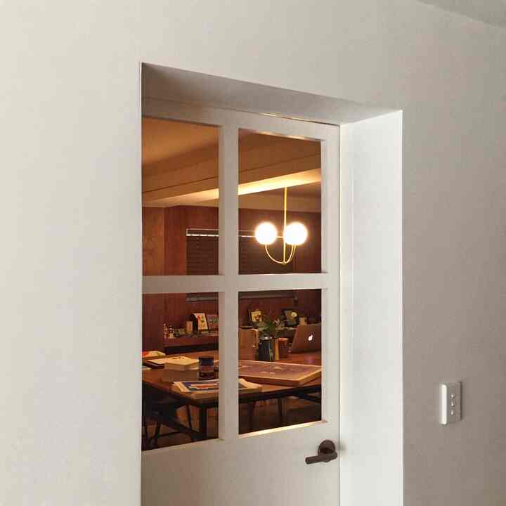 A white and brown toned dining room seen through glass-panel door, featuring a dining table and pendant light creating a cozy atmosphere