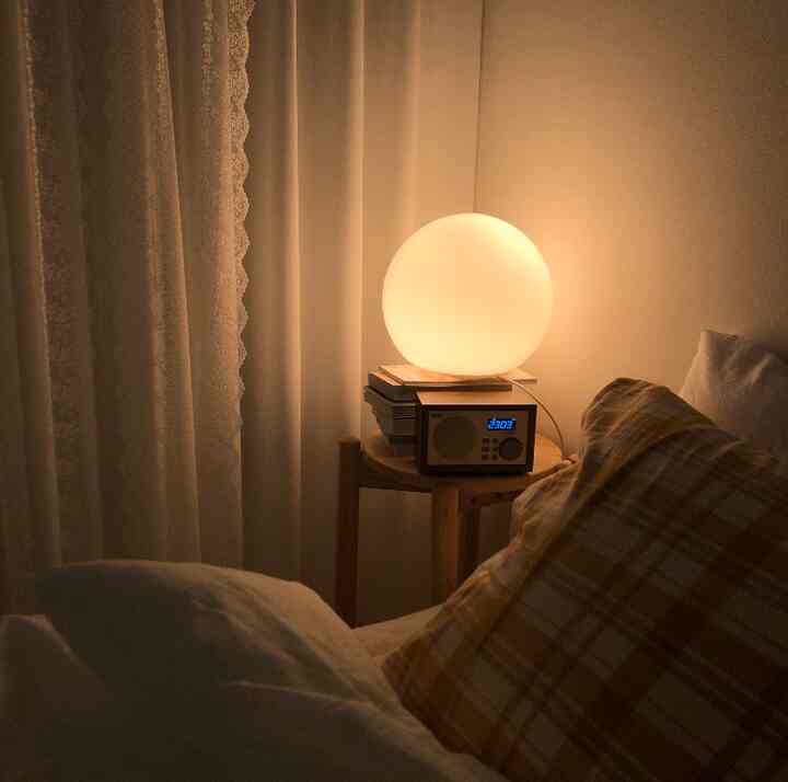 Cozy bedroom in warm brown and yellow tones, featuring a wooden stool with a mood lamp and Bluetooth radio