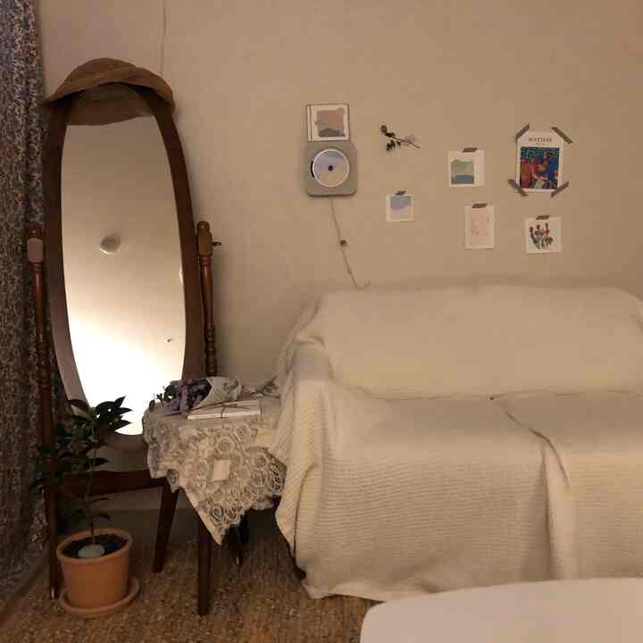 ナチュラルな色調のリビング、木製の鏡と白いソファ、植物や複数のポスターが配置された雰囲気のあるインテリア