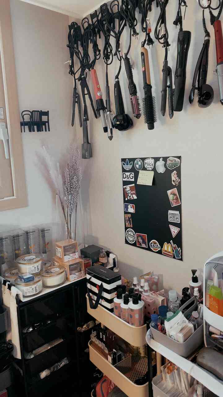 ベージュと黒の色調の狭い空間、壁に掛けられたヘアスタイリングツールと複数の収納に整理された化粧品があるナチュラルな化粧台のインテリア