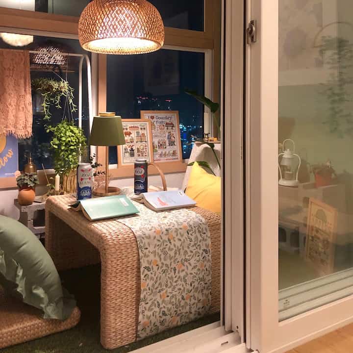 ナチュラルな雰囲気のバルコニー、ラタン家具と植物が配置され、温かみのある照明で落ち着いた空間