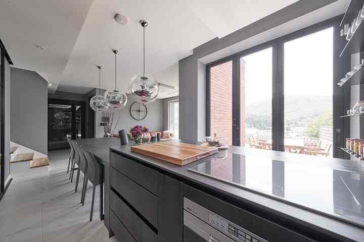 グレーと黒を基調としたモダンなキッチンとダイニングルーム、大きな窓とバルコニーが繋がる洗練された空間
