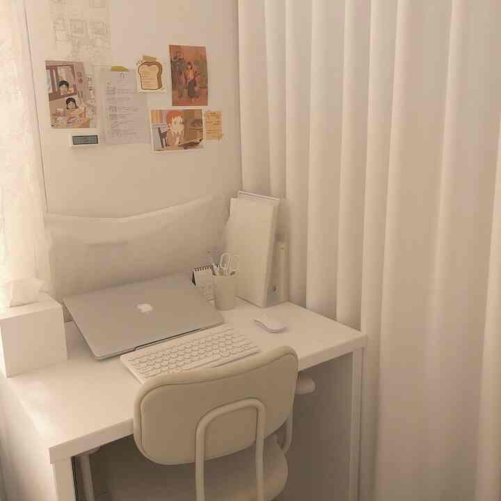 A calm white-toned small home office featuring a simple desk, chair, and blackout curtains creating a cozy workspace