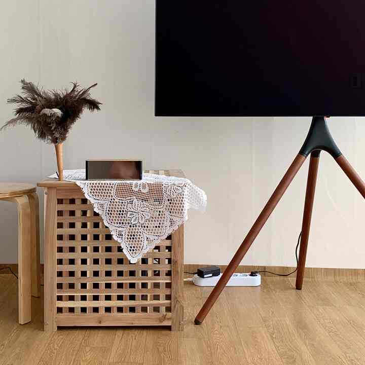 Natural wood-toned living room featuring tripod wooden TV stand, wooden basket and stool with a clean, spacious feel