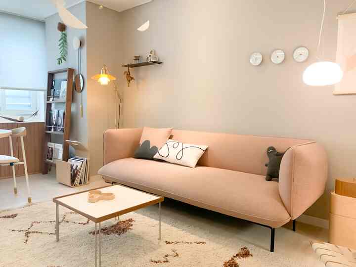 柔らかいベージュとライトブラウンのトーンでまとめられた北欧風リビング、ピンクの3人掛けソファとシンプルなトレイテーブルが配置された雰囲気のある空間