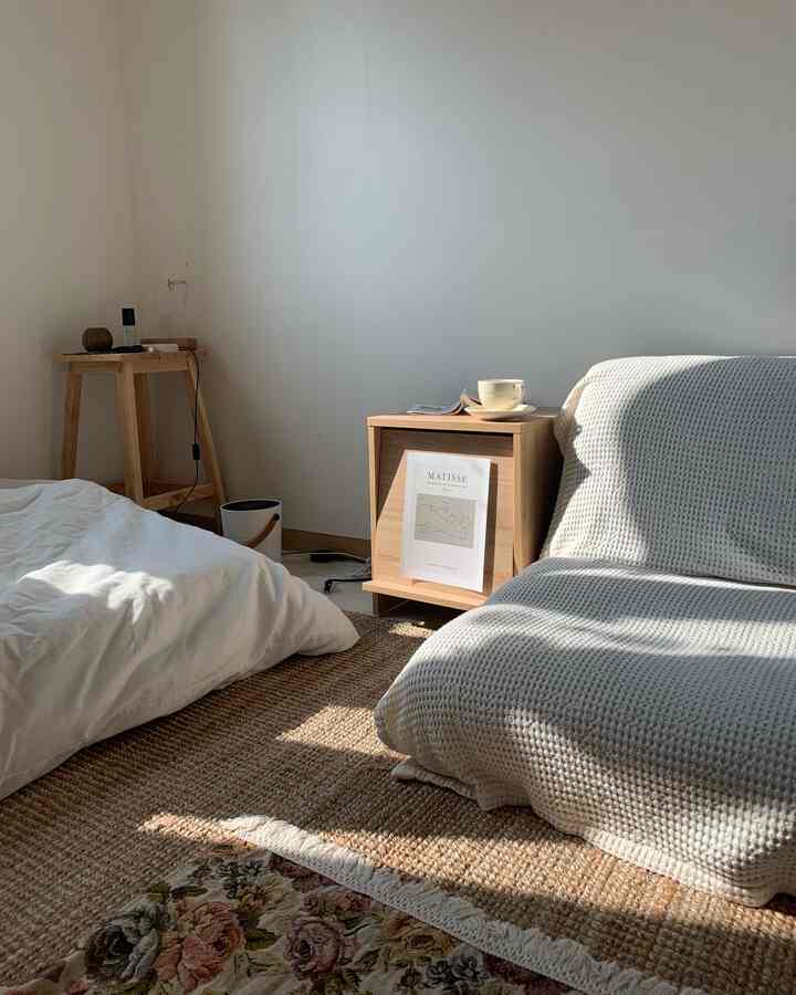 A natural tone and white studio bedroom featuring a sofa bed, nightstand, and wooden stool creating a cozy atmosphere.