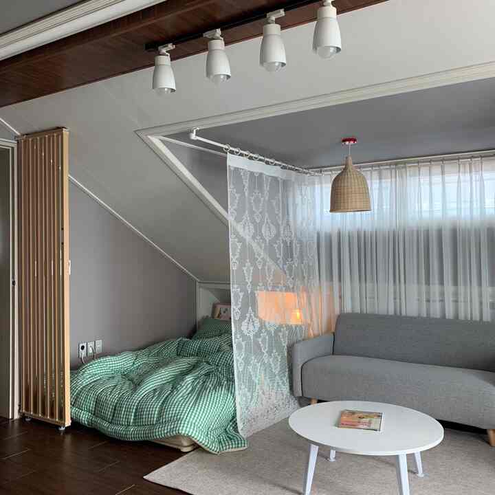 A natural-toned loft living space featuring a gray sofa, white round table, and green checkered bedding, creating a cozy atmosphere with wood elements