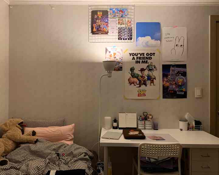 白い壁とデスク、チェック柄のベッド、犬のぬいぐるみがあるシンプルな一人暮らしの部屋