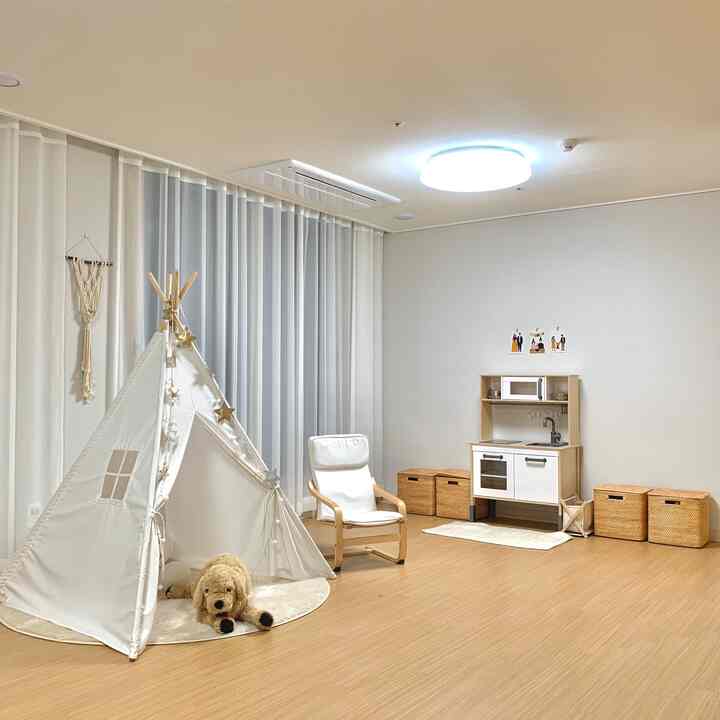 ホワイトと木目調の調和した子供部屋、テントやままごとキッチン、アームチェアと収納バスケットが配された雰囲気のある空間