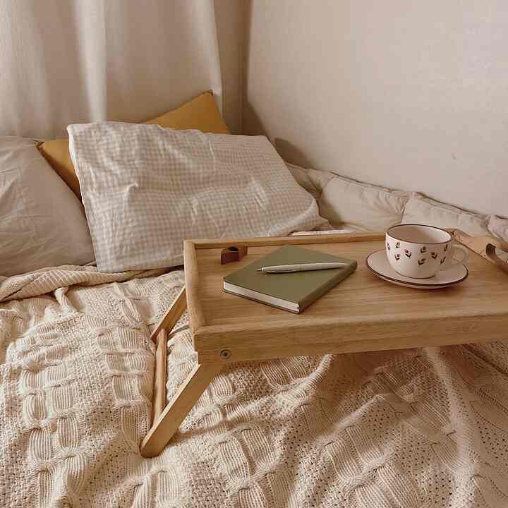Natural-tone bedroom featuring a wooden bed tray, knit blanket, and pillows creating a cozy and comfortable atmosphere