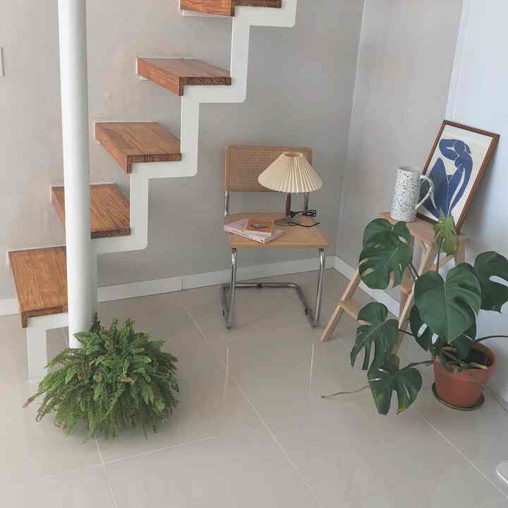 Natural toned small space under stairs featuring a rattan chair, table lamp and plants creating a cozy corner