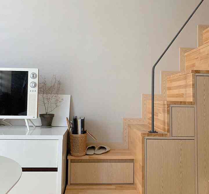 White and light brown toned living room featuring wooden stairs and TV stand, embodying a simple natural modern interior