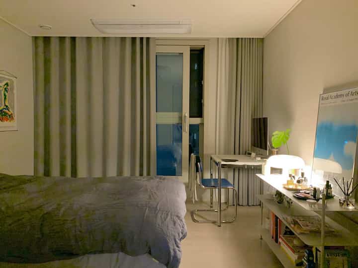 Gray and white toned bedroom featuring a bed centrally and a desk with lighting on the right, creating a calm atmosphere