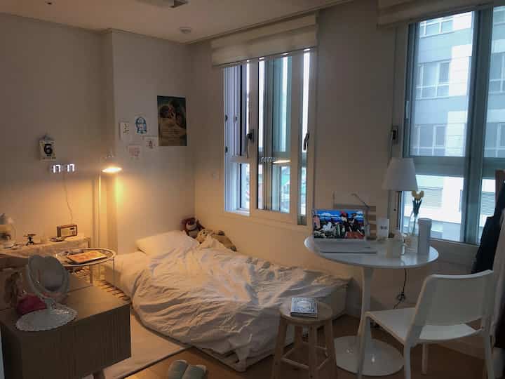 Cozy studio bedroom in white and wood tones featuring a small round table and soft natural lighting