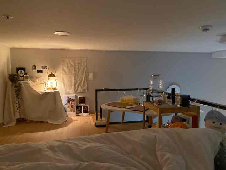 Cozy single bedroom with warm wood tones and white accents, featuring ambient lighting, a desk, and artistic decor