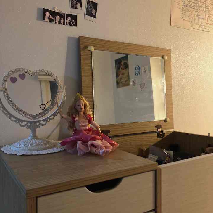 A beige-toned small vanity space featuring a wooden-framed mirror, a doll, and a heart-shaped table lamp creating a cozy atmosphere
