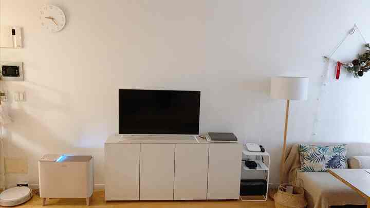 Bright white and natural toned living room featuring a TV stand, floor lamp, and beige sofa creating a cozy atmosphere