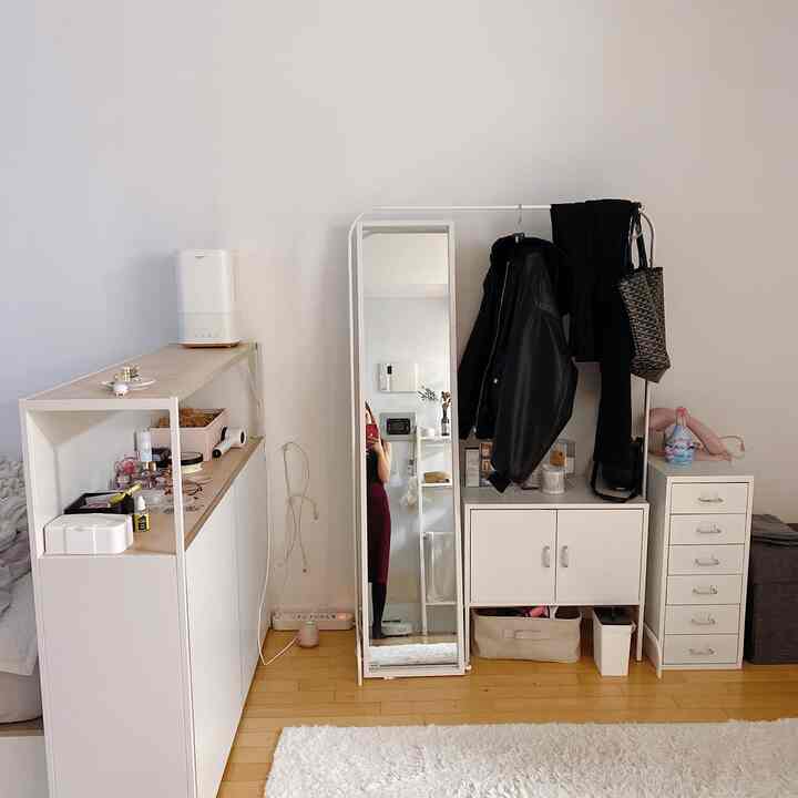 ホワイトとウッドトーンの小さな玄関スペース、収納家具と全身鏡、コートラックが配置されたシンプルなインテリア