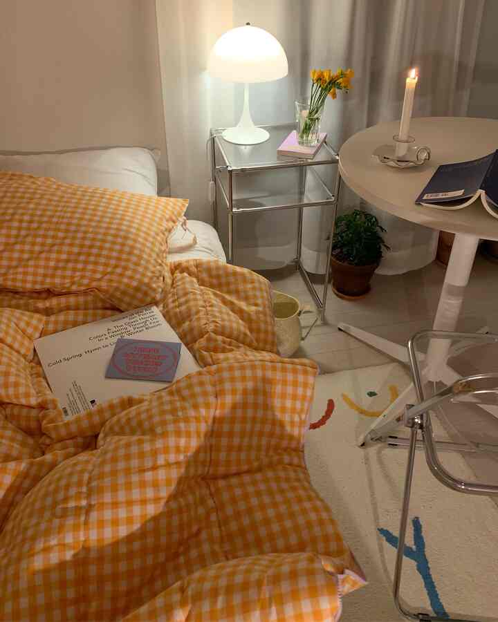 Cozy bedroom with orange gingham bedding and a transparent chair, featuring warm lighting and a small vase centerpiece