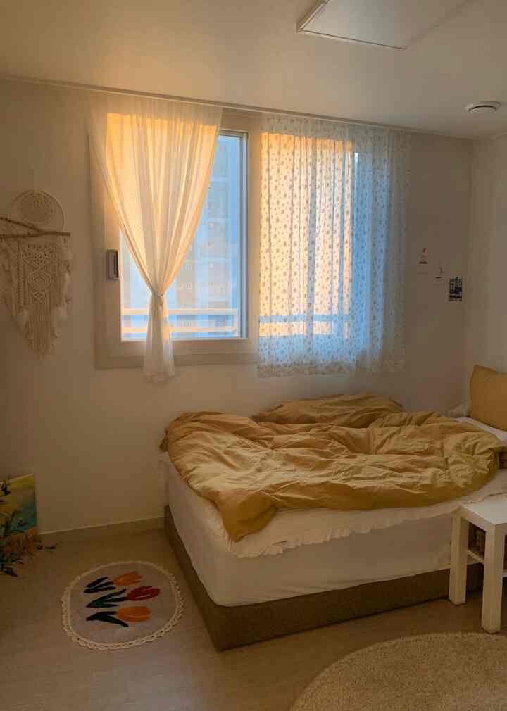 暖かいベージュとホワイトのトーンの寝室、柄の異なるカーテンと快適なベッドが配置された雰囲気のあるヴィンテージインテリア