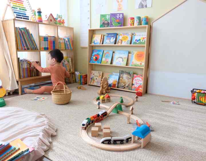 ベージュの色調の子供部屋、木製本棚と汽車のおもちゃが配置された温かみのある自然な印象のプレイルーム