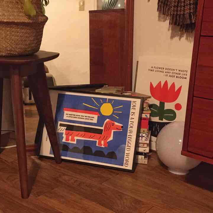 Cozy interior with warm wood tone flooring and reddish-brown furniture, featuring a dog illustration and flower posters