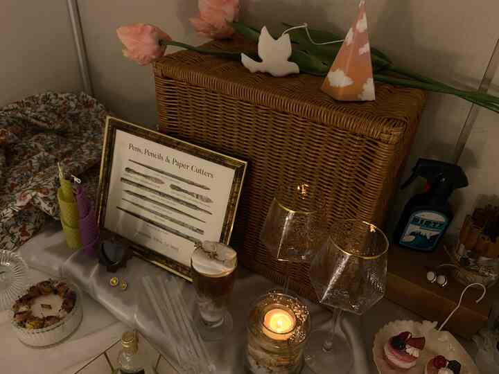 Cozy interior space featuring a warm brown rattan basket, gold-rimmed wine glasses, lit candle, flower vase, and picture frame as decorative elements