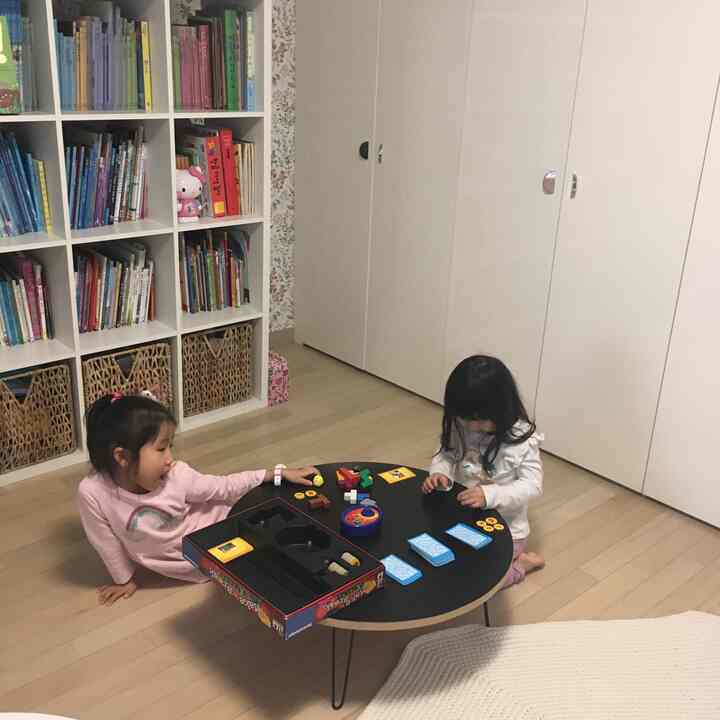 Wood-tone floored kids' room with white bookshelves, featuring a black round table where children are playing cards