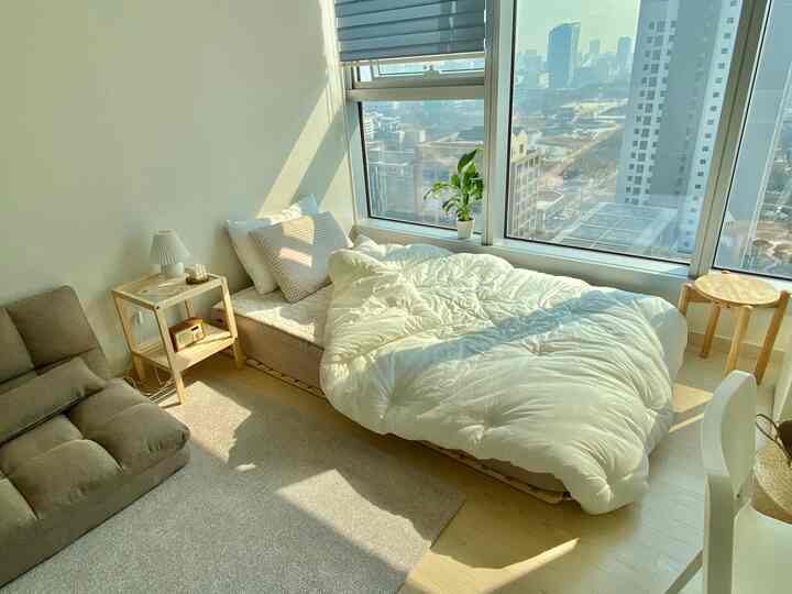 A white and natural tone studio bedroom featuring a bed by the window and a sofa bed, creating a cozy harmonious space