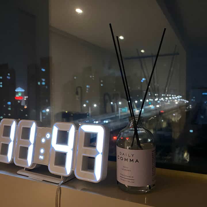 White and black toned window ledge space featuring a LED clock and diffuser against the cozy night view of an elevated highway