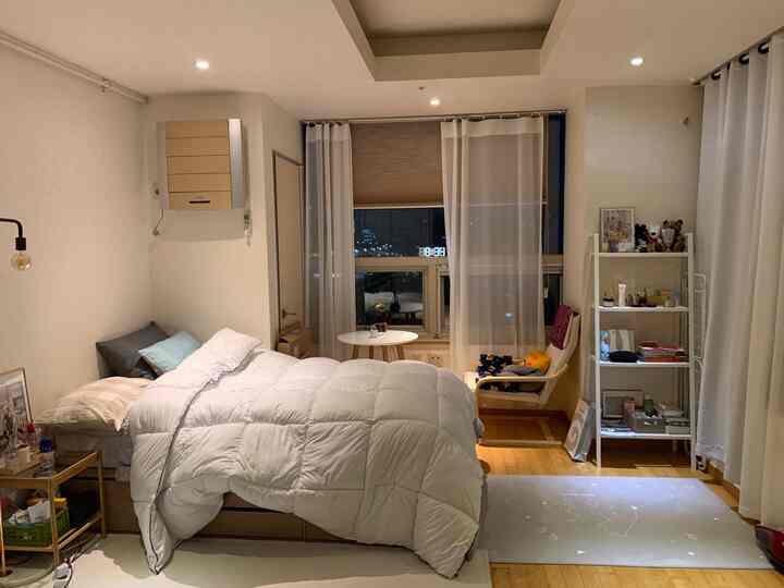 Cozy single bedroom in white and beige tones featuring bed, nightstand, curtains, and an armchair in a relaxed setting