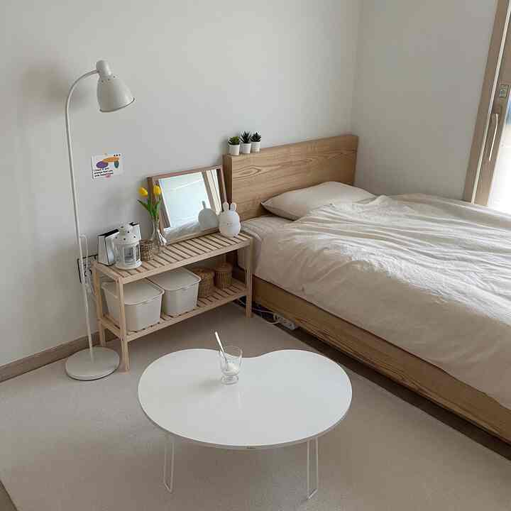 白と木目調のワンルーム寝室、木製ベッドとテーブル、フロアランプが配置された洗練されたミニマルな空間