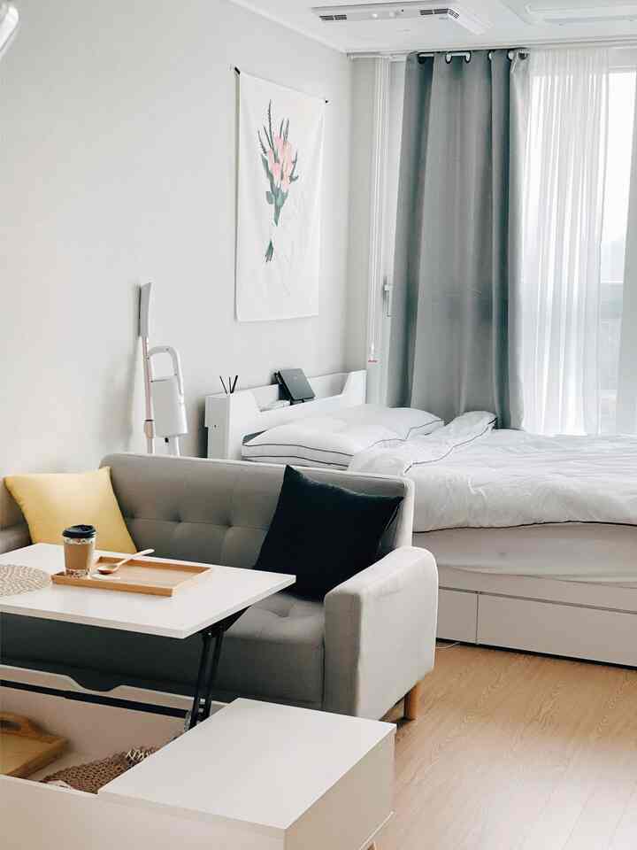White and gray toned studio apartment featuring a lift table, sofa, and bed in a cozy compact space