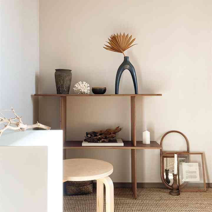 Natural-toned workspace featuring wooden shelves, light wood stool, and neatly arranged objets creating a simple setting