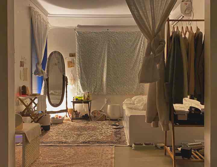 White-toned vintage studio apartment featuring Persian Kazaar carpet, full-length mirror, and nightstand with cozy atmosphere