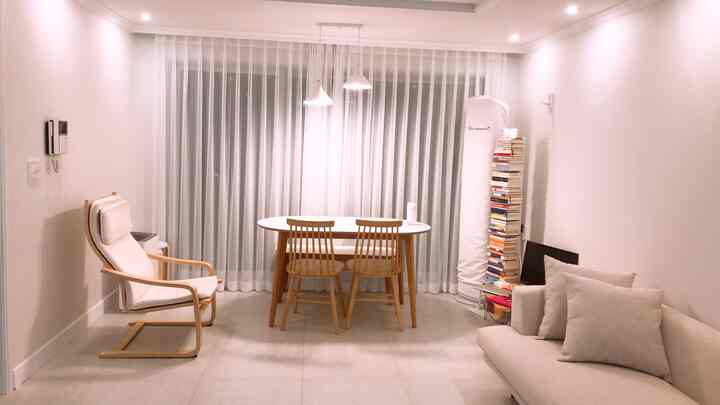 白と木目調のリビング、シアーカーテンとダイニングテーブル、ソファが配置された居心地の良いシンプルなインテリア