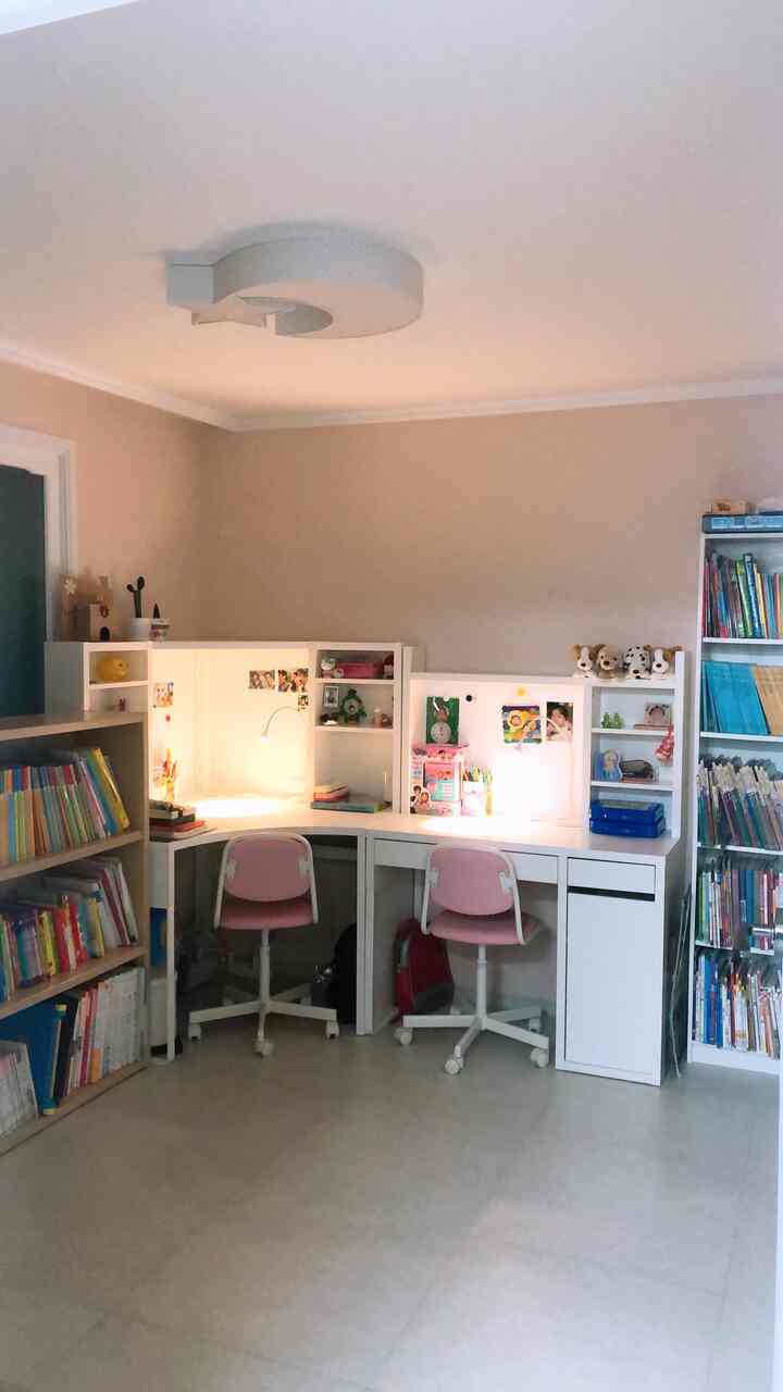Soft white and pink toned kids' room with two desks and bookshelves arranged in a cozy study space