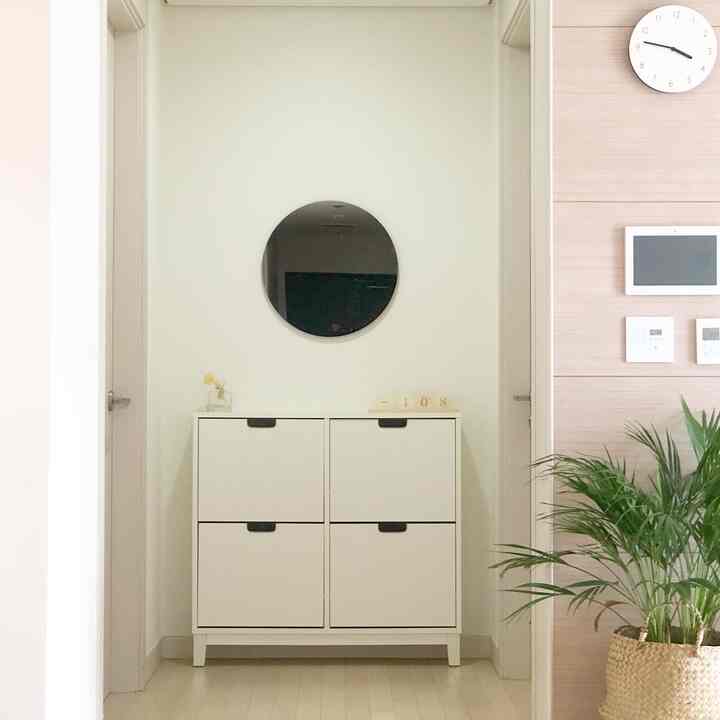 明るくナチュラルカラーの壁と床、中央にシンプルなホワイトのIKEAシューズラックと丸い鏡が配置されたモダンな空間