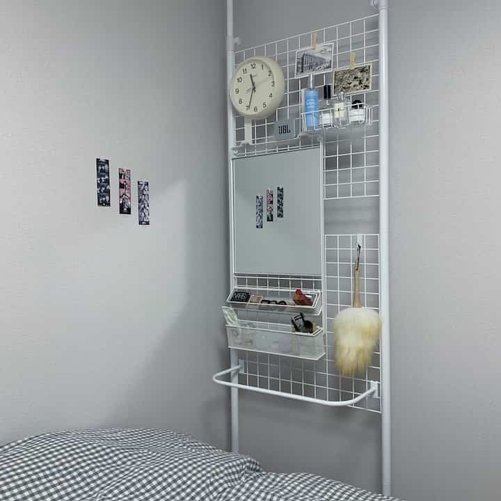 ホワイトとグレーのトーンのコンパクトな寝室、パーティションの化粧台と静かな時計が配置された落ち着いた空間