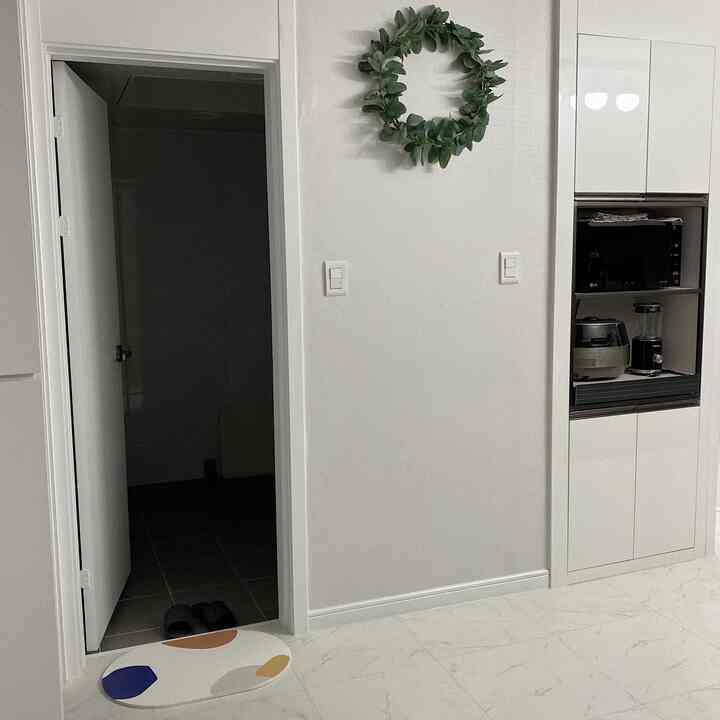 White-toned kitchen with an open restroom entrance, featuring a diatomaceous earth bath mat and clean modern design