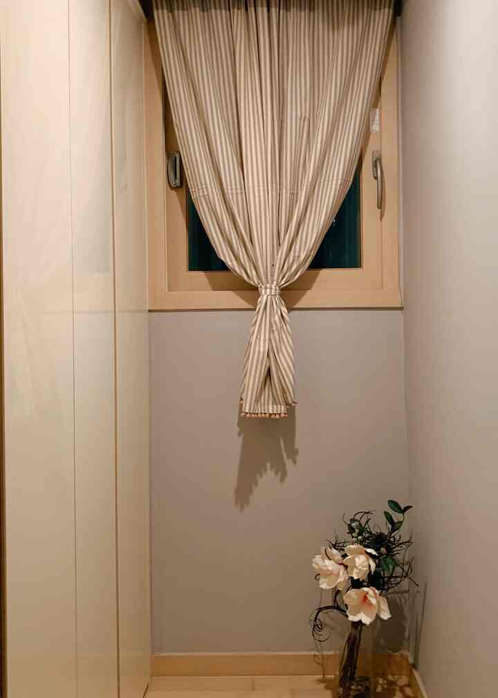 ベージュと木目調のウォークインクローゼット、中央にストライプのカーテン、右下に花の飾りがあるシンプルな空間