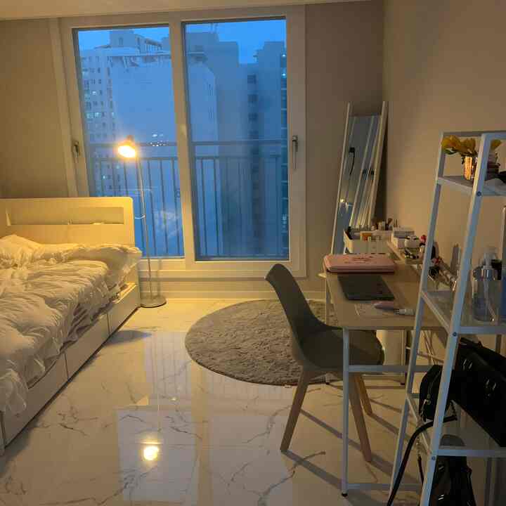 A white and gray toned single household bedroom with floor lamp by the window, featuring desk, full-length mirror, and rug in a cozy space